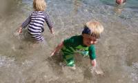 To børn. De står i vandet på stranden. De plasker rundt og leger.