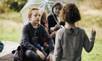 Fire børn snakker sammen i en gruppe under en paraply.