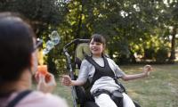 Pige i en kørestol smiler til en voksen som blæser sæbebobler.