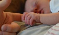 Nyfødt baby med lukkede øjne holder med hele sin hånd rundt om en voksens pegefinger